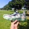 A hand holds up an Altra Torin 6 running shoe with light mint green upper, navy blue laces and mint green sole, photographed outdoors in a sunny park with green grass and large trees in the background
