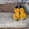 A pair of Mizuno Wave Rider 24 in bright golden yellow with black accents and white sole, placed on weathered concrete steps waiting to be adopted