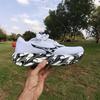 White Mizuno Wave Rider 30 with a black-and-white swirl-patterned midsole, held up on an open palm in a sunny park with tall eucalyptus trees.