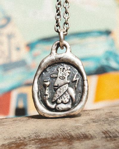 An oval silver pendant with an embossed bearded Zeus holding a lightning bolt, on a heavy silver chain.