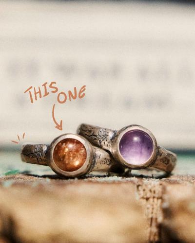 Two textured silver rings with round stones; a hand-drawn arrow marked “this one” points to the orange sunstone.