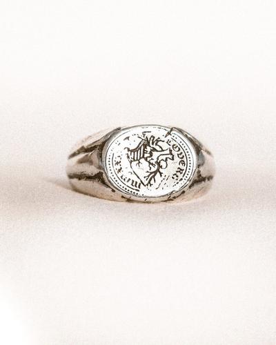 A recycled-silver signet ring with an engraved round coin-like face, on a pale background.